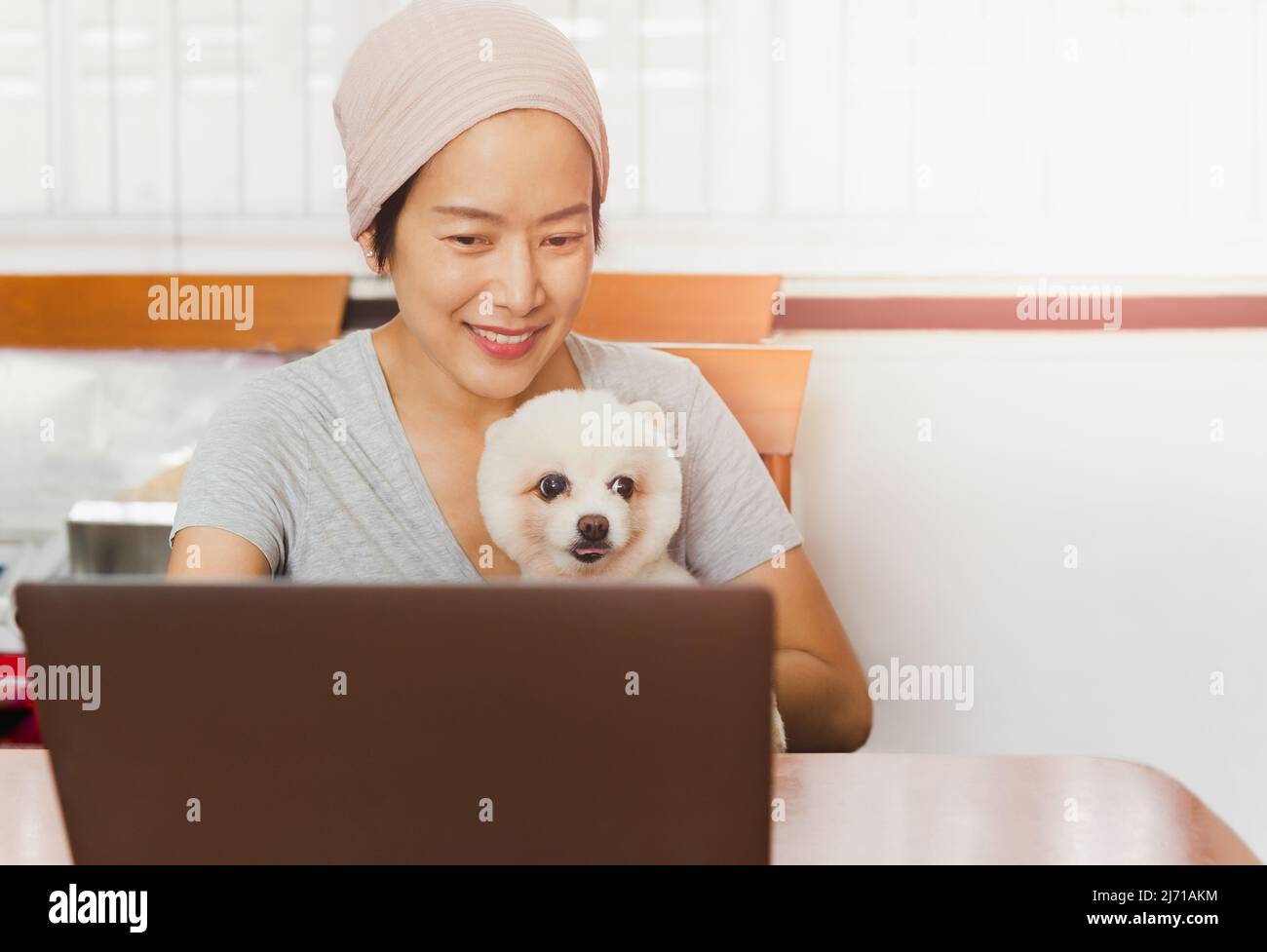 Donna freelancer caucasica che tiene il suo cane Pomerania mentre lavora sul laptop a casa. Foto Stock