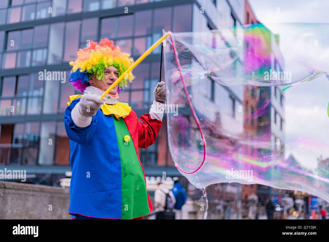 Gdansk,PL-16 Mar 22: Clown creando enormi e luminose bolle di sapone nell'aria. Pagliaccio colorato che offre intrattenimento per passare attraverso le persone su Foto Stock