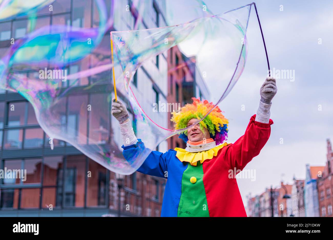 Gdansk,PL-16 Mar 22: Clown creando enormi e luminose bolle di sapone nell'aria. Pagliaccio colorato che offre intrattenimento per passare attraverso le persone su Foto Stock