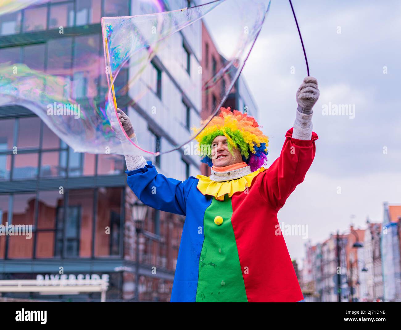 Gdansk,PL-16 Mar 22: Clown creando enormi e luminose bolle di sapone nell'aria. Pagliaccio colorato che offre intrattenimento per passare attraverso le persone su Foto Stock