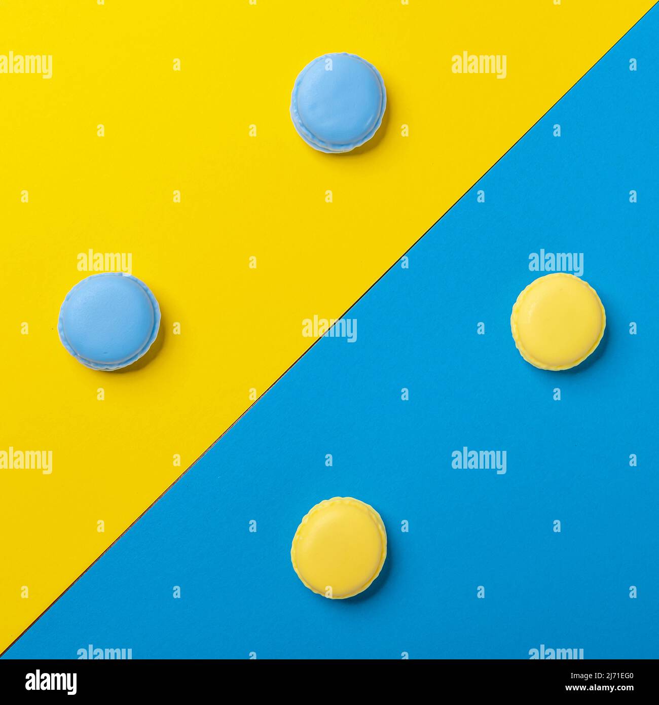 I macaron blu e giallo sono disposti simmetricamente su uno sfondo di colore opposto Foto Stock