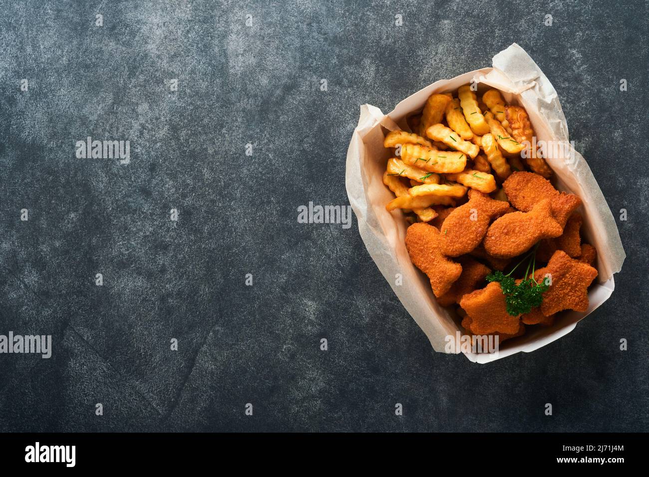 Fish and chips fast food britannico. Bastoncini di pesce con patatine fritte su piastra di carta da asporto su fondo di cemento vecchio e scuro. Tradizionale inglese authe Foto Stock