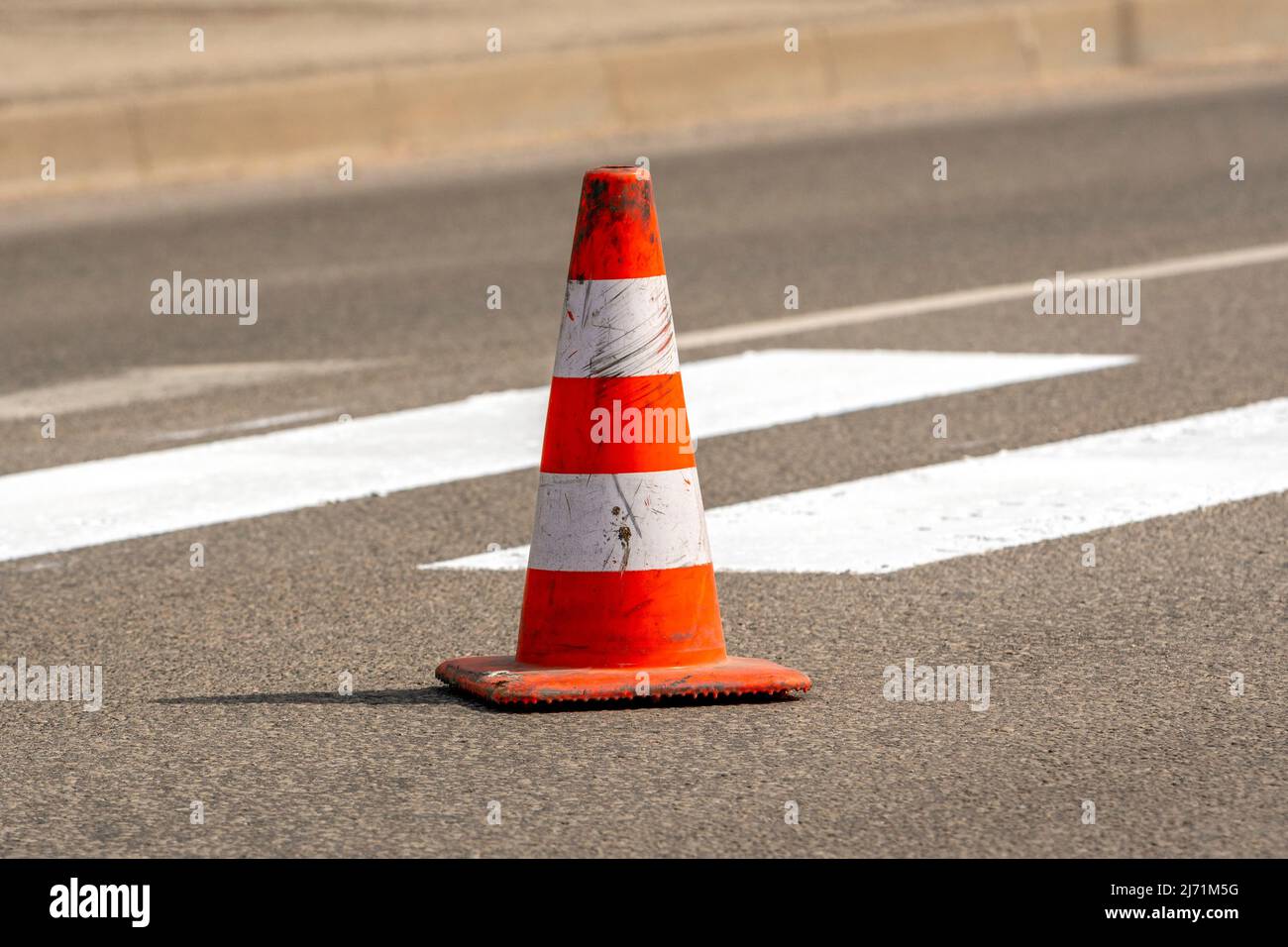 Cono stradale con strisce arancioni e bianche in piedi su strada su asfalto grigio durante i lavori di costruzione di strade. Appena dipinte linee di strada bianche su pedes Foto Stock