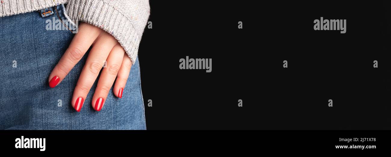Mano femminile con bel manicure - chiodi rossi su jeans tessuto denim e sfondo nero con banner spazio copia. Testata panoramica larga Foto Stock