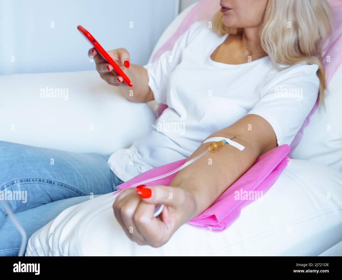 Donna donatore guardando il telefono cellulare mentre l'ago è nel braccio , Closeup del braccio con l'ago inserito nel braccio Foto Stock