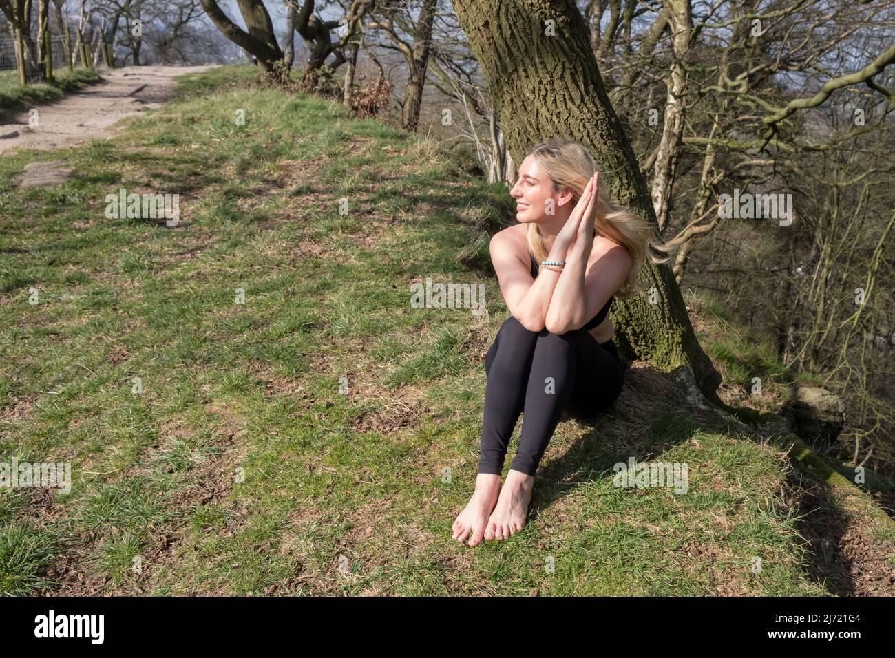 Bella donna che pratica yoga all'aperto sotto gli alberi Foto Stock