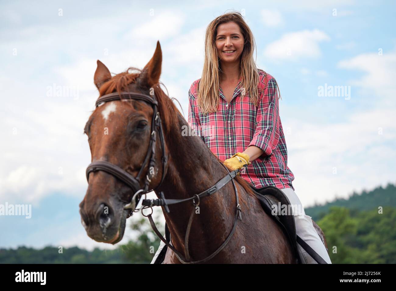 Giovane donna in camicia che riposa sul cavallo marrone - il cappotto bagnato dal sudore - dopo aver cavalcato, sorridente Foto Stock