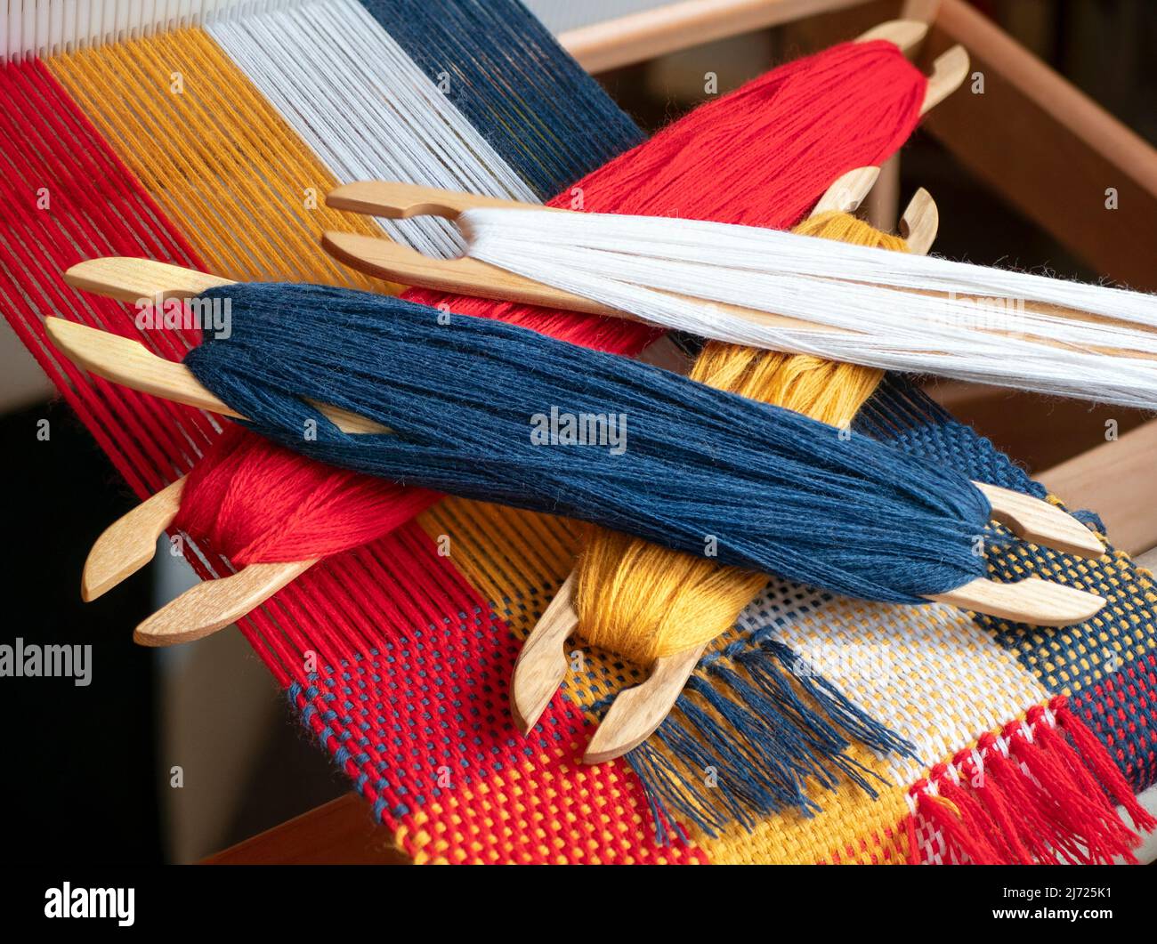Esempio di tessitura tabby. Navette a bastone di legno con filo colorato sul telaio a mano. Produzione tessile Foto Stock