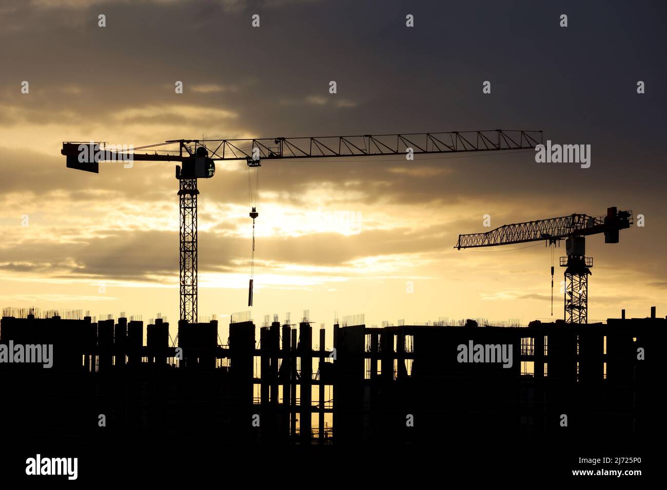 Sagome di gru a torre e lavoratori su ponteggi di edificio incompiuto all'alba. Edilizia abitativa, condominio in città sullo sfondo Foto Stock