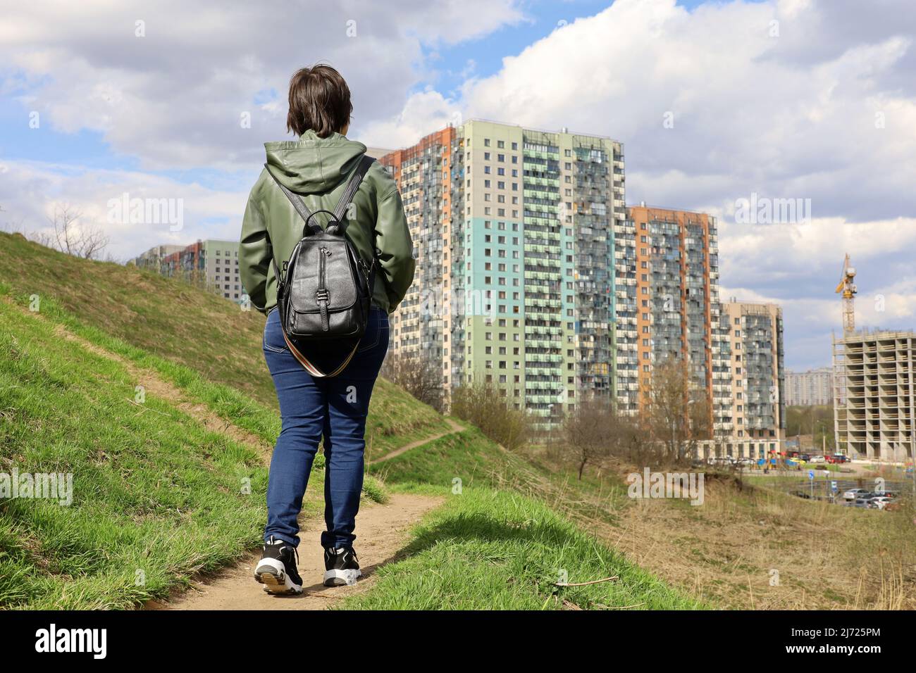 Donna guarda le nuove case in piedi su verde collina, paesaggio urbano in primavera. Settore edile e concetto immobiliare Foto Stock