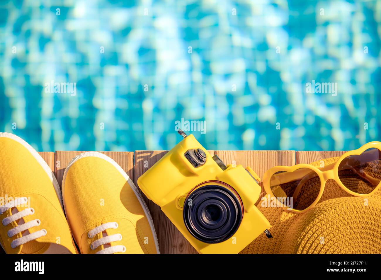 Sneakers gialli e macchina fotografica su legno blu contro sfondo d'acqua. Concetto di vacanza estiva e di viaggio Foto Stock
