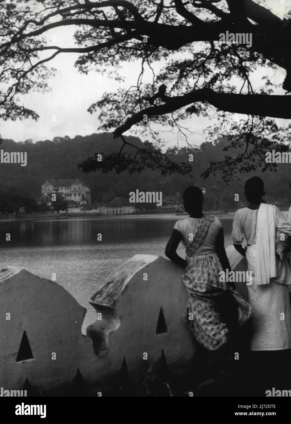 Il tour reale: Ceylon - Lago di Kandy -- la Regina di H.M. e la R.H. il Duca di Edimburgo visiterà Kandy dal 18th al 20th aprile 1954. La città di Kandy si trova in una valle tra le colline, ed è a se stessa ad un'altitudine di circa 1500 piedi. Questo lago artificiale si trova proprio accanto alla città. Alcune donne native si fermino presso la balaustra, guardando attraverso l'acqua fino al "Tempio del dente". Una vista del Lago Kandy, guardando di fronte al 'Tempio del dente.' Aprile 12, 1954. (Foto di Rosemary Gilliat, Camera Press). Foto Stock