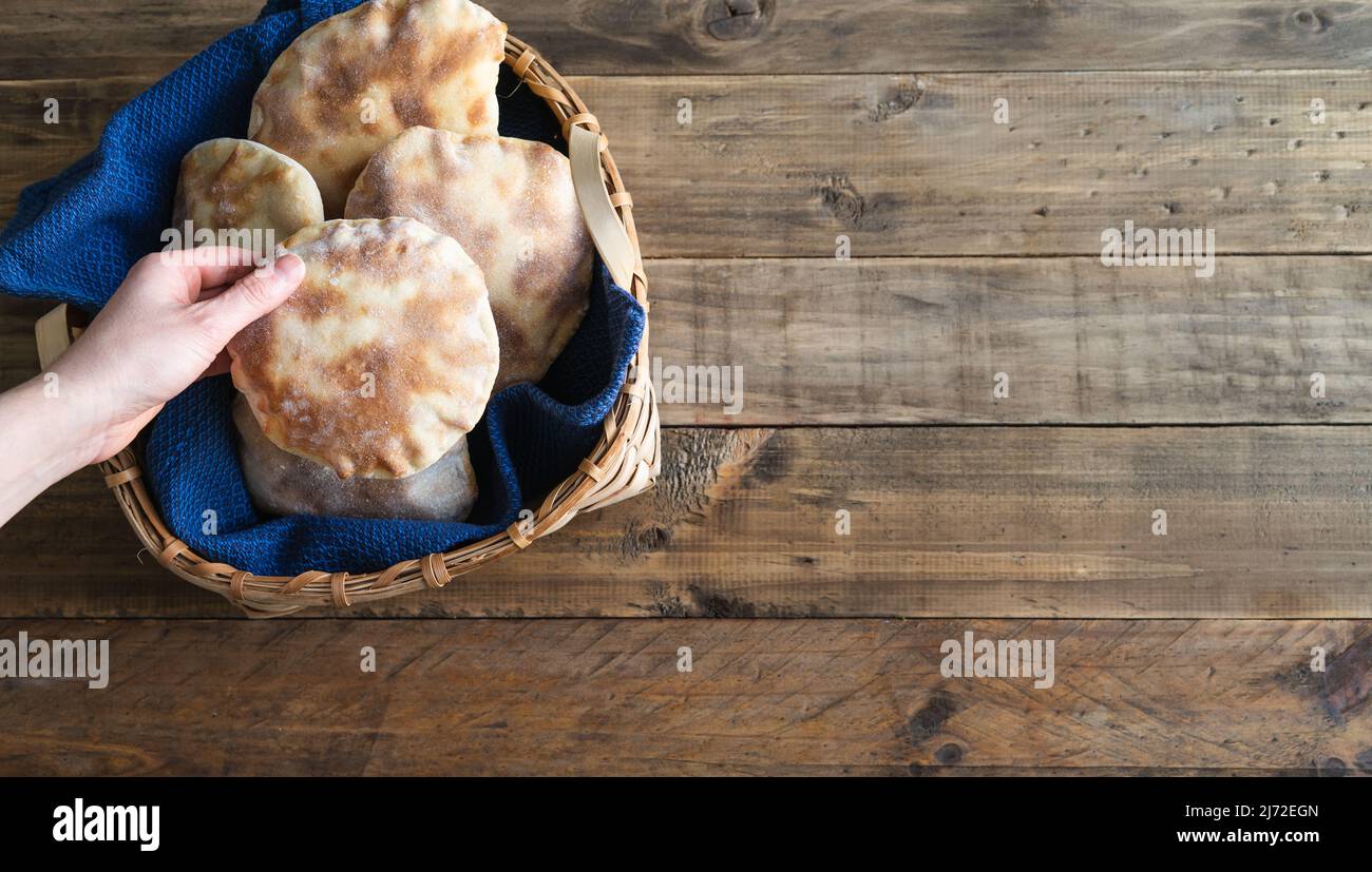 Le mani della donna collocano il pane della pita fatto in casa in un cestino di legno sul vecchio tavolo di legno. Spazio di copia. Foto Stock