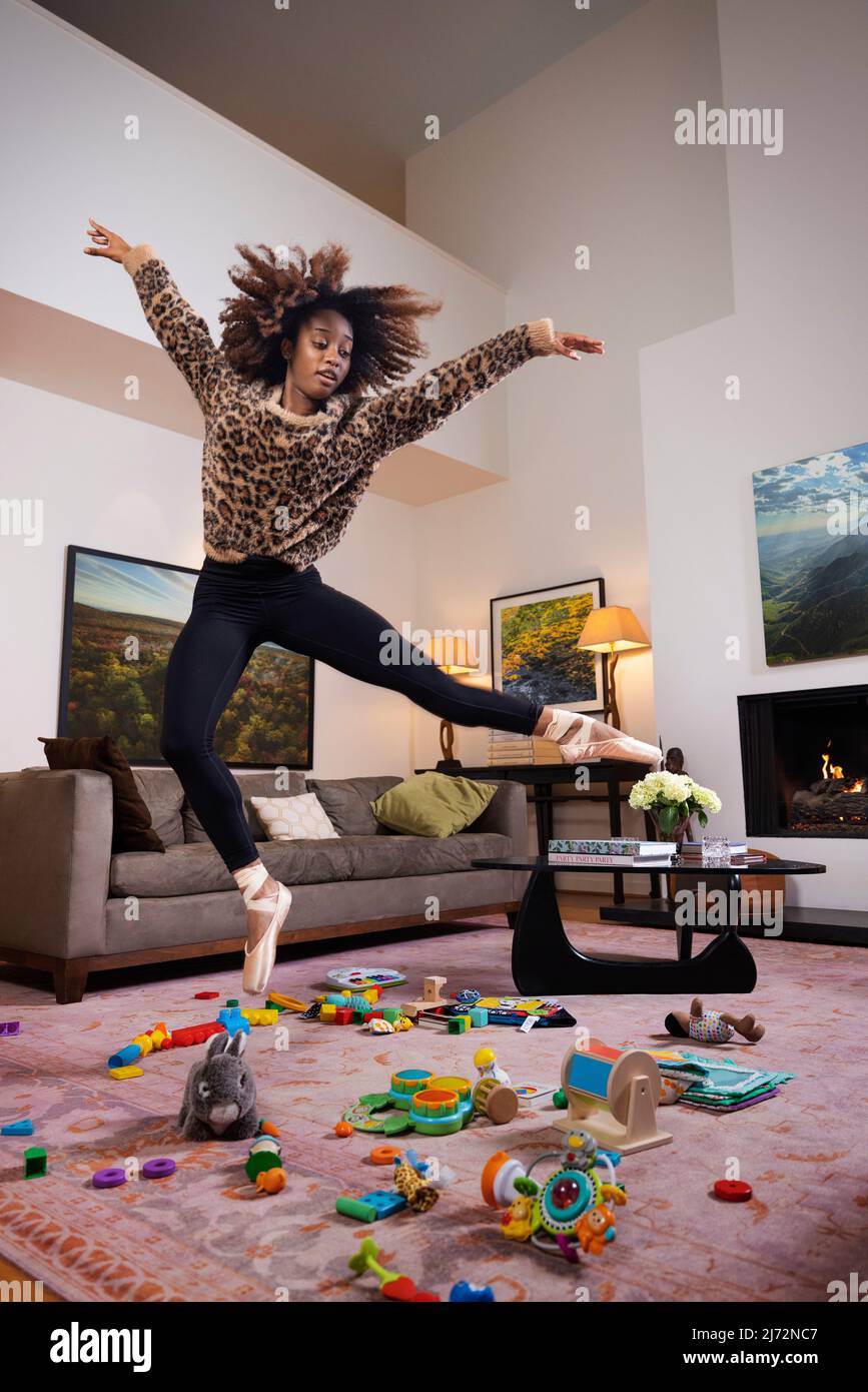 Ballerina femminile che salta sul mare di giocattoli in un soggiorno. Foto Stock