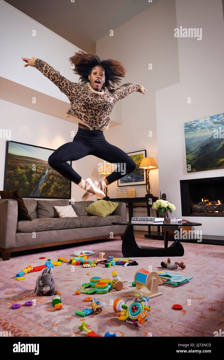 Ballerina femminile e giovane madre che saltano sopra i giocattoli sparsi sul pavimento Foto Stock