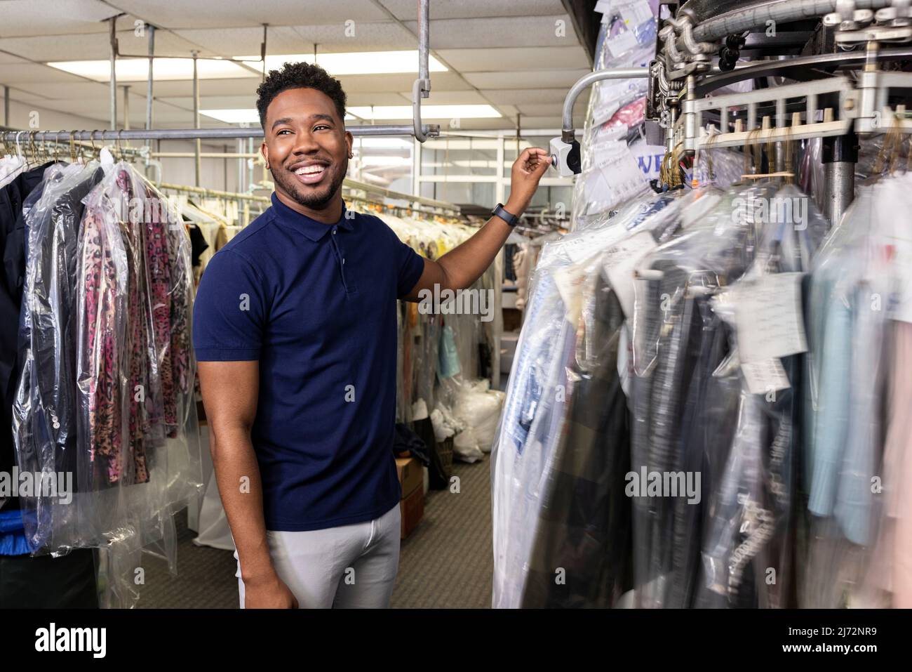 Giovane uomo nero sorridente mentre tira i panni dal rack per il cliente a secco Foto Stock