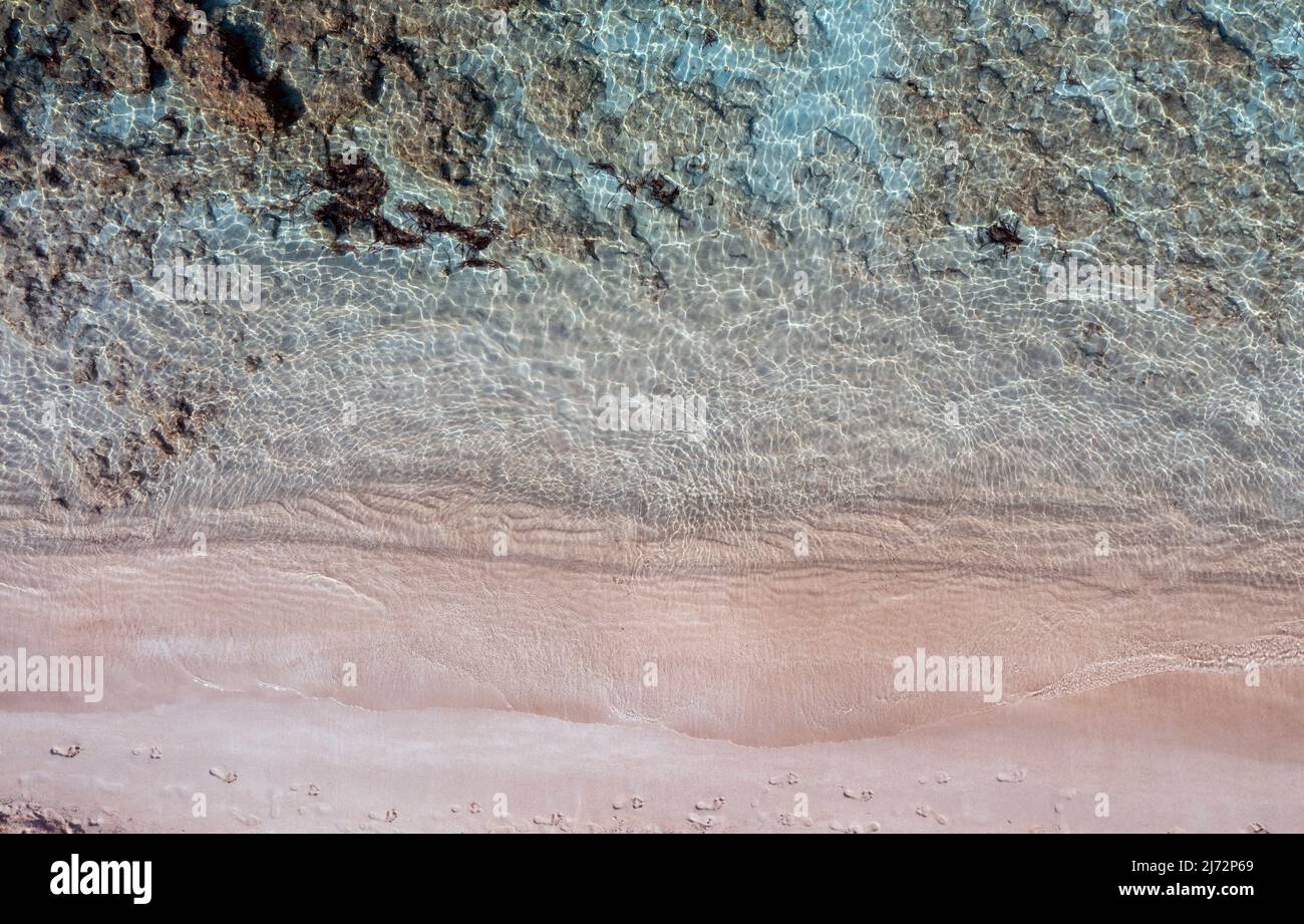 Spiaggia di sabbia, blu turchese vista dall'alto mare. Impronte su sabbia rosa bagnata. Acqua limpida e trasparente, fondo marino roccioso. Somma dell'isola greca dell'Egeo Foto Stock