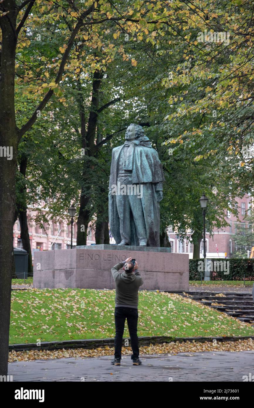 Uomo che scatta una foto della statua del poeta e giornalista finlandese Eino Leino a Esplanade Park, Helsinki, Finlandia. Foto Stock