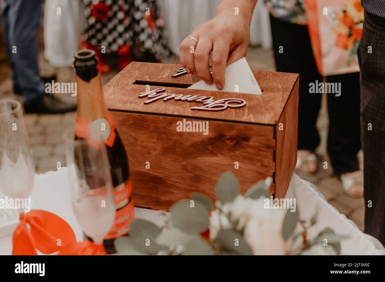 una mano dell'uomo mette una busta con i soldi in una scatola di festa di nozze di legno per i regali agli sposi novelli. Tradizione russa Slavica Ucraina Foto Stock