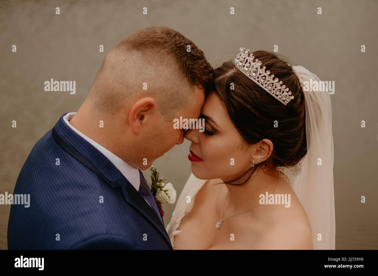 Il giovane uomo biondo caucasico europeo sposa in abito blu e donna dai capelli neri sposa in abito da sposa bianco con velo lungo e tiara sulla testa. Sposi novelli Foto Stock