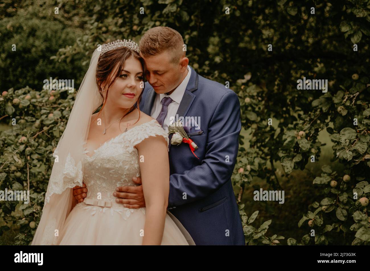 Il giovane uomo biondo caucasico europeo sposa in abito blu e donna dai capelli neri sposa in abito da sposa bianco con velo lungo e tiara sulla testa. Sposi novelli Foto Stock