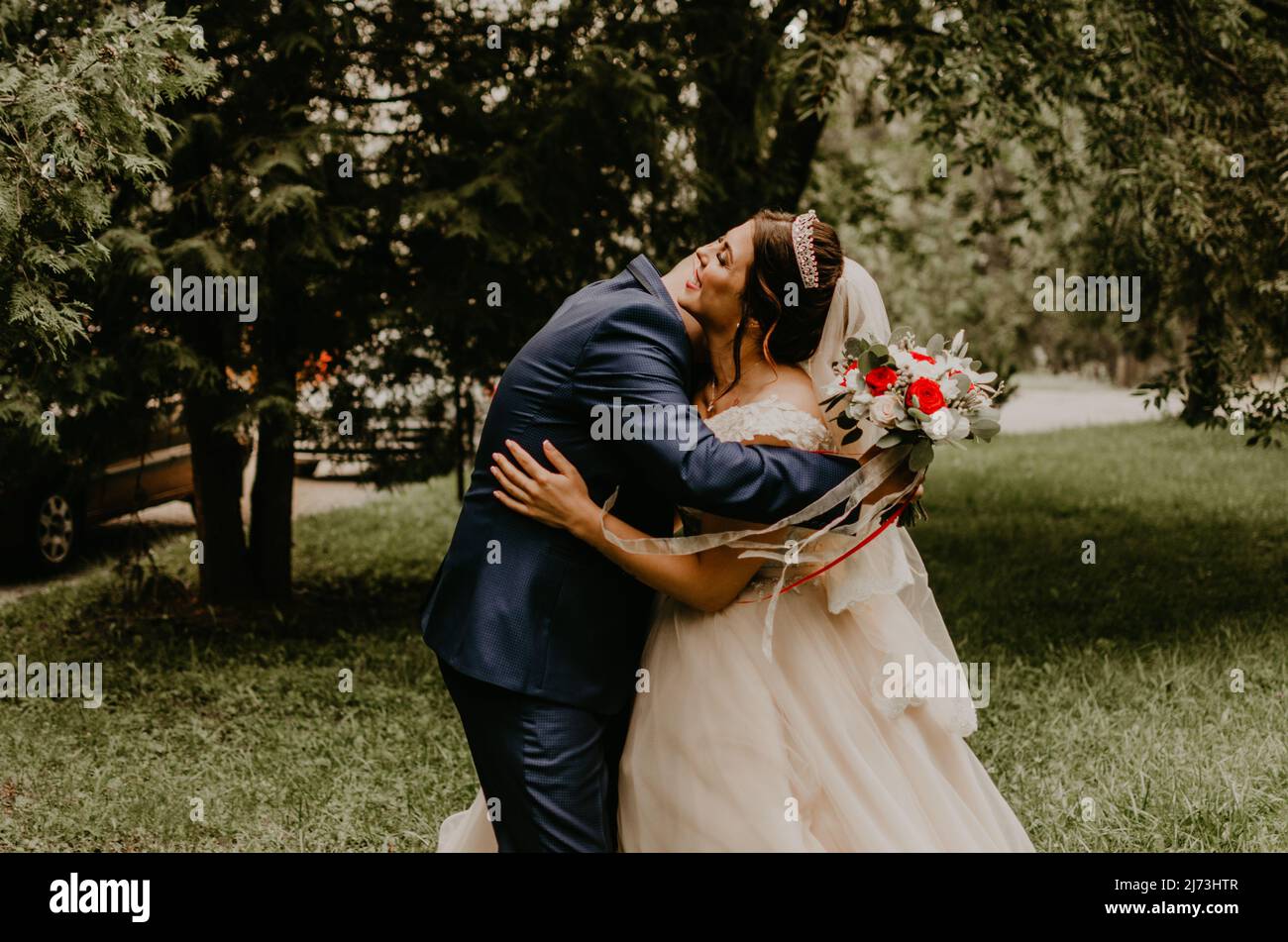 Il giovane uomo biondo caucasico europeo sposa in abito blu e donna dai capelli neri sposa in abito da sposa bianco con velo lungo e tiara sulla testa. Prima Foto Stock