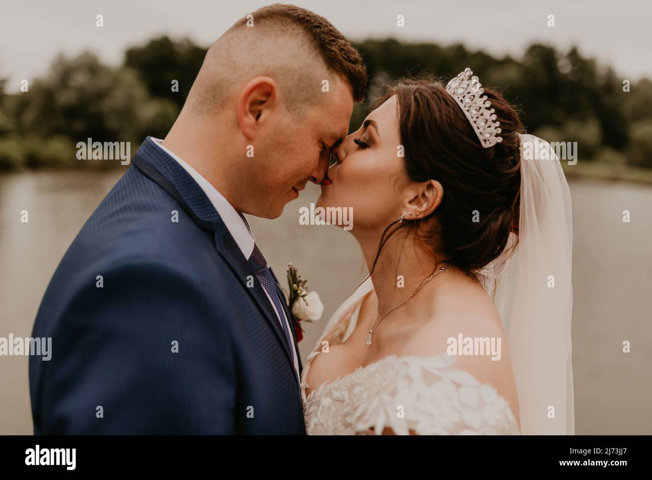 Il giovane uomo biondo caucasico europeo sposa in abito blu e donna dai capelli neri sposa in abito da sposa bianco con velo lungo e tiara sulla testa. Sposi novelli Foto Stock