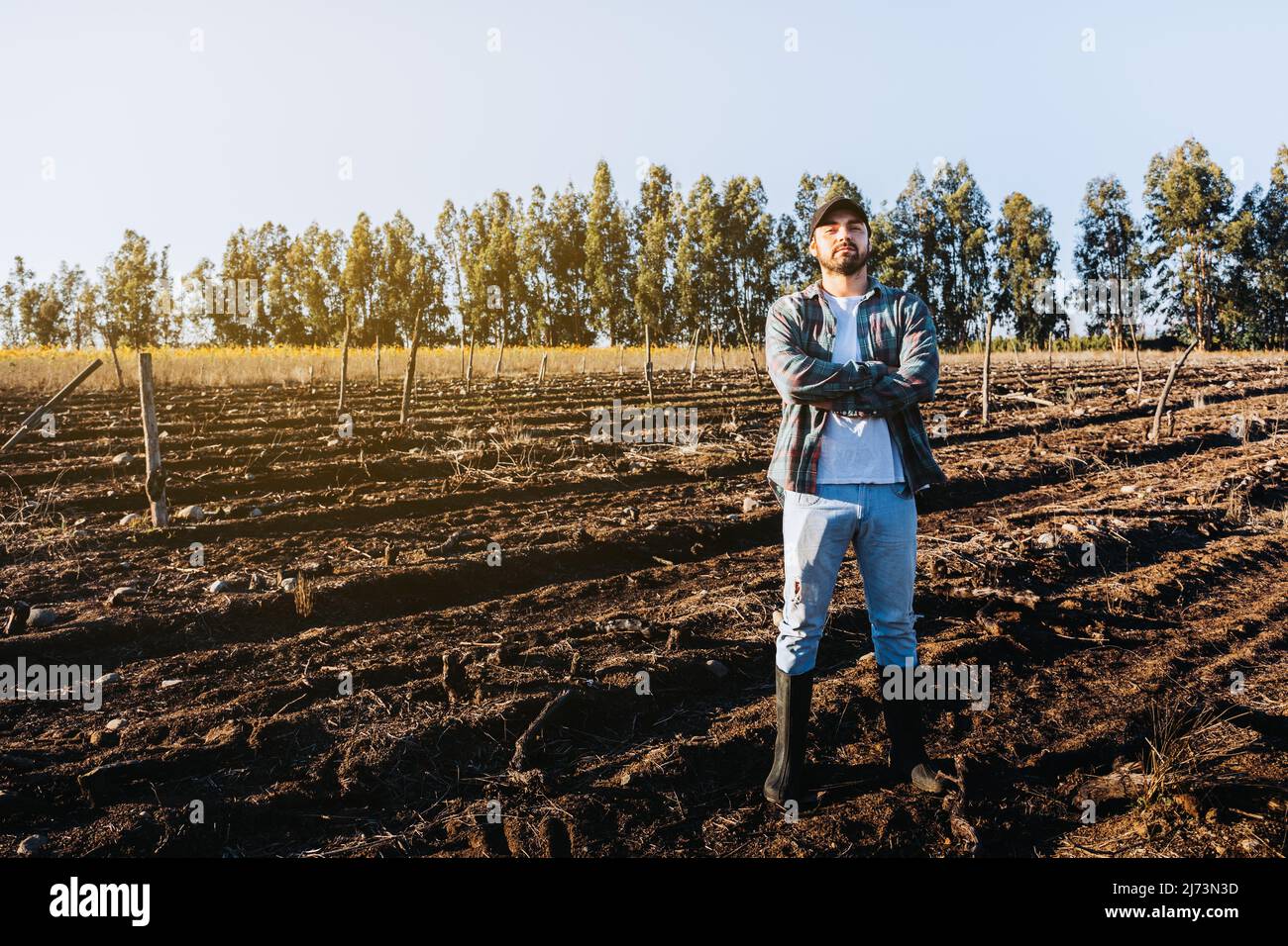 Giovane contadino latino a braccia incrociate in mezzo al terreno agricolo. Concetto di sostenibilità agricola. Foto Stock