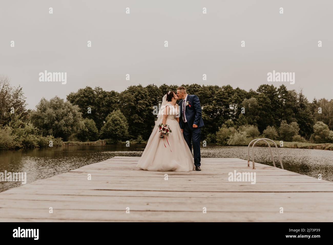 Il giovane uomo biondo caucasico europeo sposa in abito blu e donna dai capelli neri sposa in abito da sposa bianco con velo lungo e tiara sulla testa. Sposi novelli Foto Stock