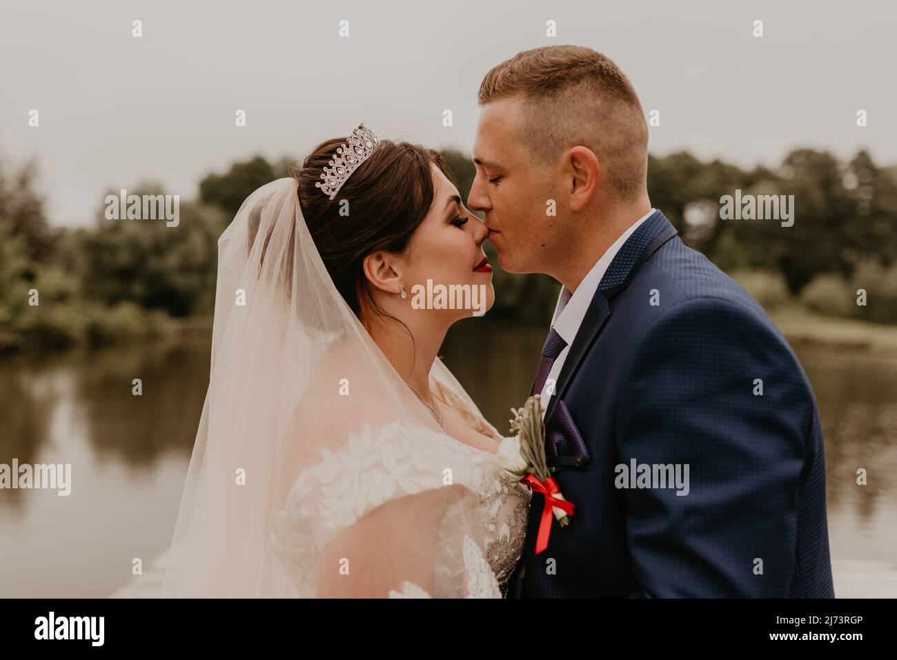 Il giovane uomo biondo caucasico europeo sposa in abito blu e donna dai capelli neri sposa in abito da sposa bianco con velo lungo e tiara sulla testa. Sposi novelli Foto Stock