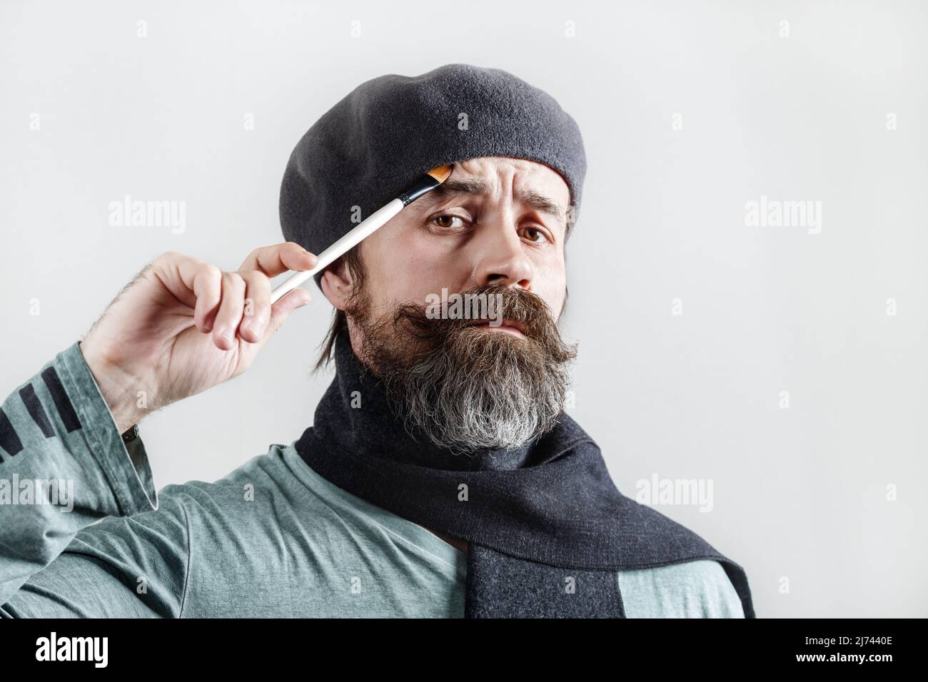 Artista barbuto premuroso. L'uomo pensivo in beretta con un pennello in mano guarda la macchina fotografica. Foto Stock