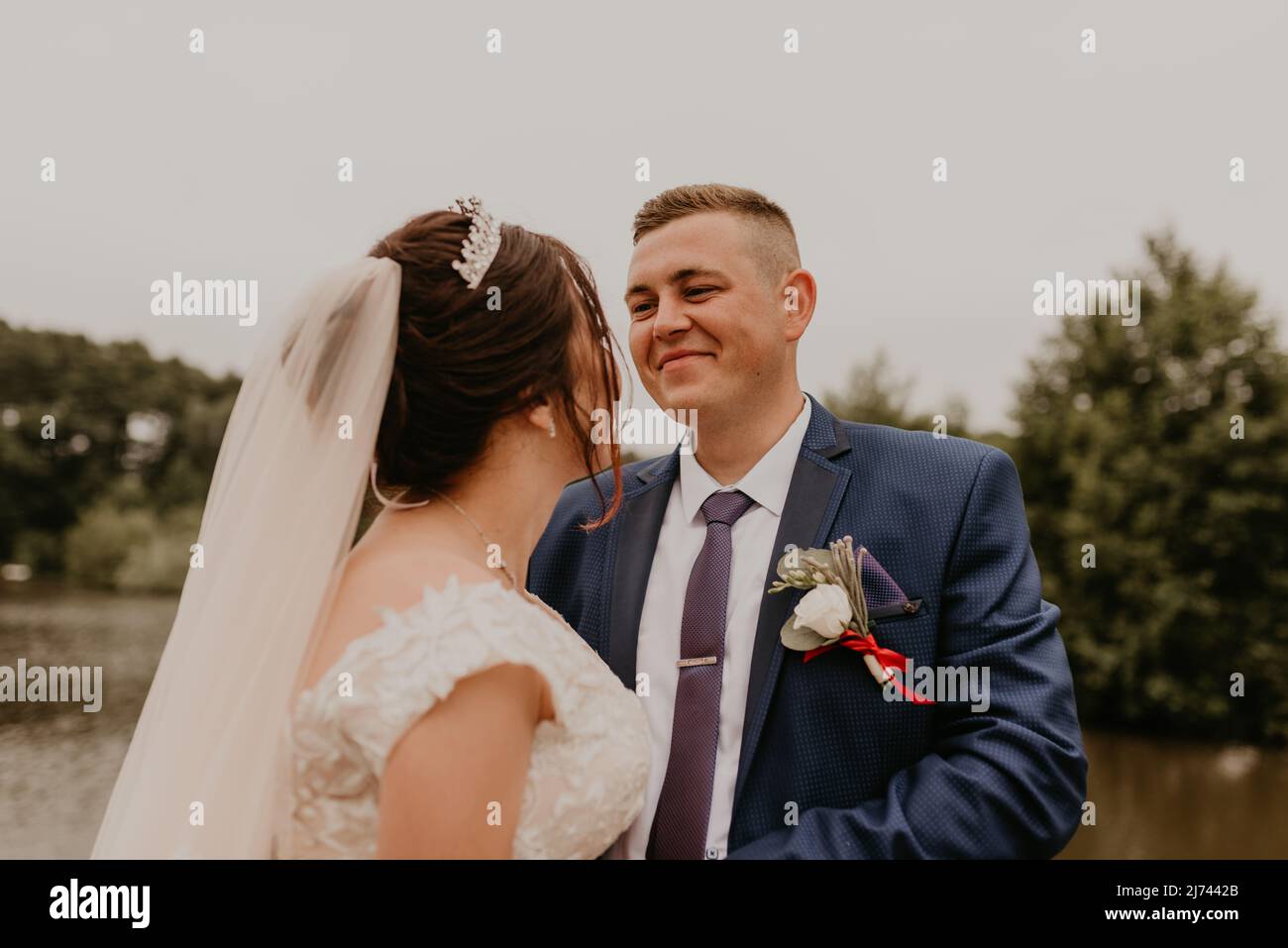 Il giovane uomo biondo caucasico europeo sposa in abito blu e donna dai capelli neri sposa in abito da sposa bianco con velo lungo e tiara sulla testa. Sposi novelli Foto Stock