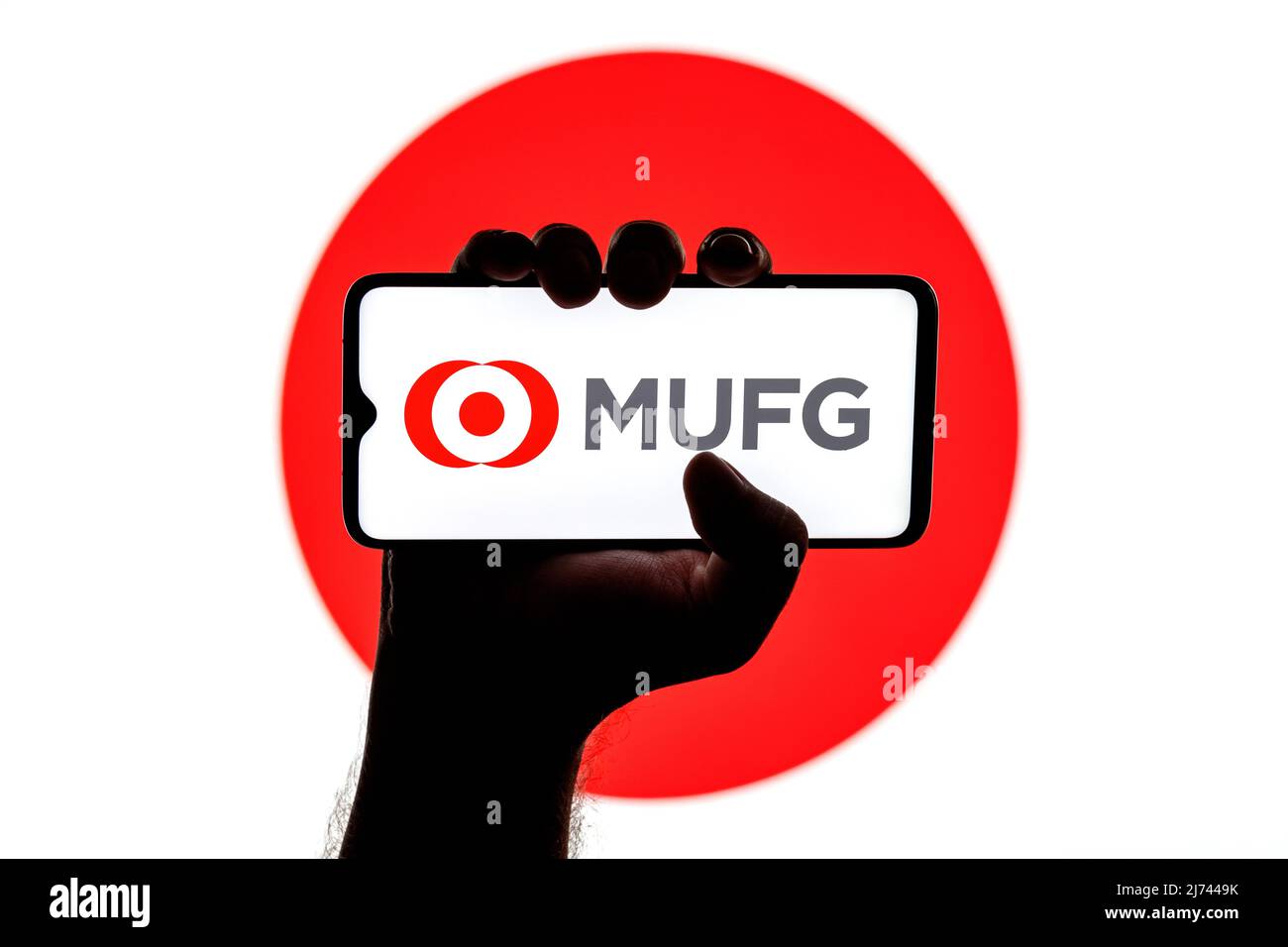 Smartphone con logo Mitsubishi UFJ Financial Group sullo schermo in mano applaiata sullo sfondo della bandiera giapponese Foto Stock