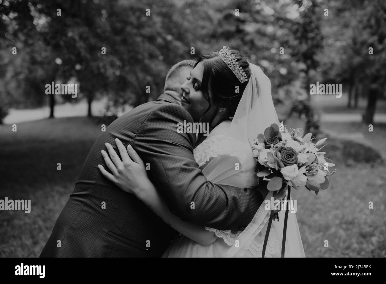 Il giovane uomo biondo caucasico europeo sposa in abito blu e donna dai capelli neri sposa in abito da sposa bianco con velo lungo e tiara sulla testa. Prima Foto Stock