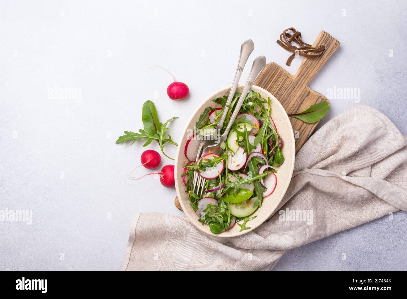 Cibo vegano sano e gustoso. Vista dall'alto di insalata leggera con ravanello, cetriolo, cipolla, foglie verdi fresche e senape sause su sfondo grigio di cemento Foto Stock