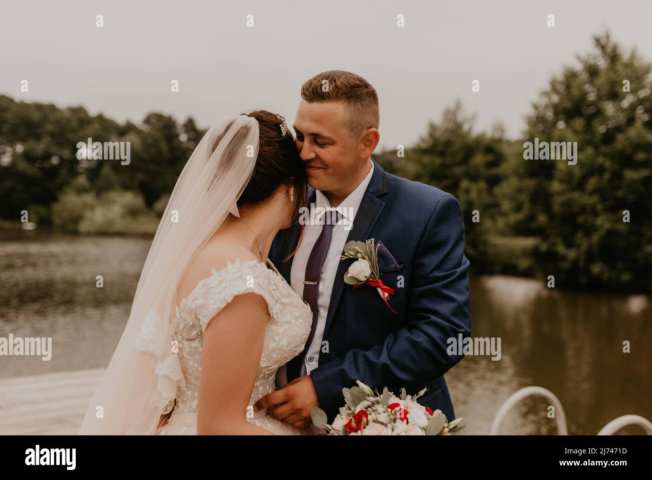 Il giovane uomo biondo caucasico europeo sposa in abito blu e donna dai capelli neri sposa in abito da sposa bianco con velo lungo e tiara sulla testa. Sposi novelli Foto Stock
