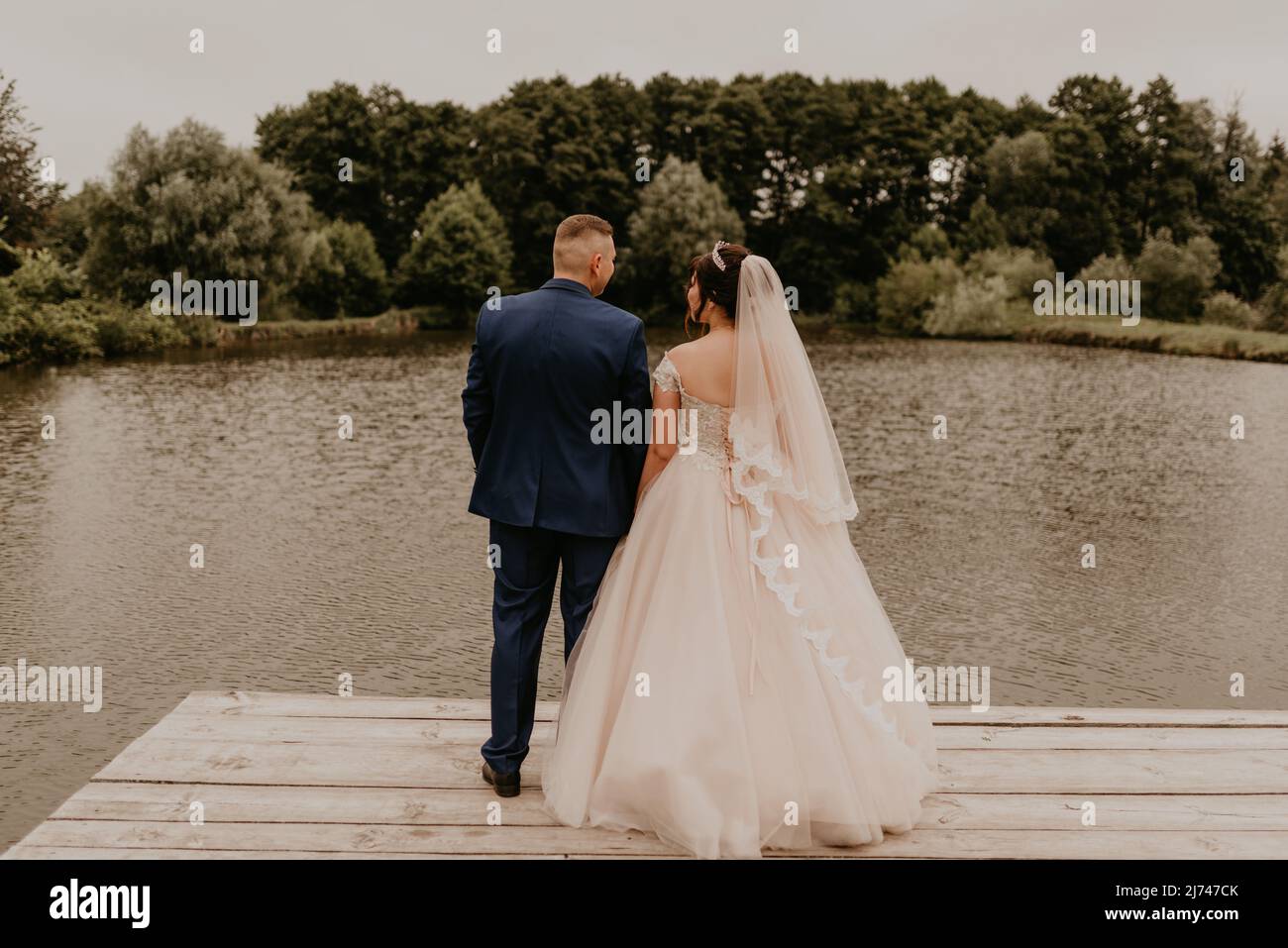 Il giovane uomo biondo caucasico europeo sposa in abito blu e donna dai capelli neri sposa in abito da sposa bianco con velo lungo e tiara sulla testa. Sposi novelli Foto Stock