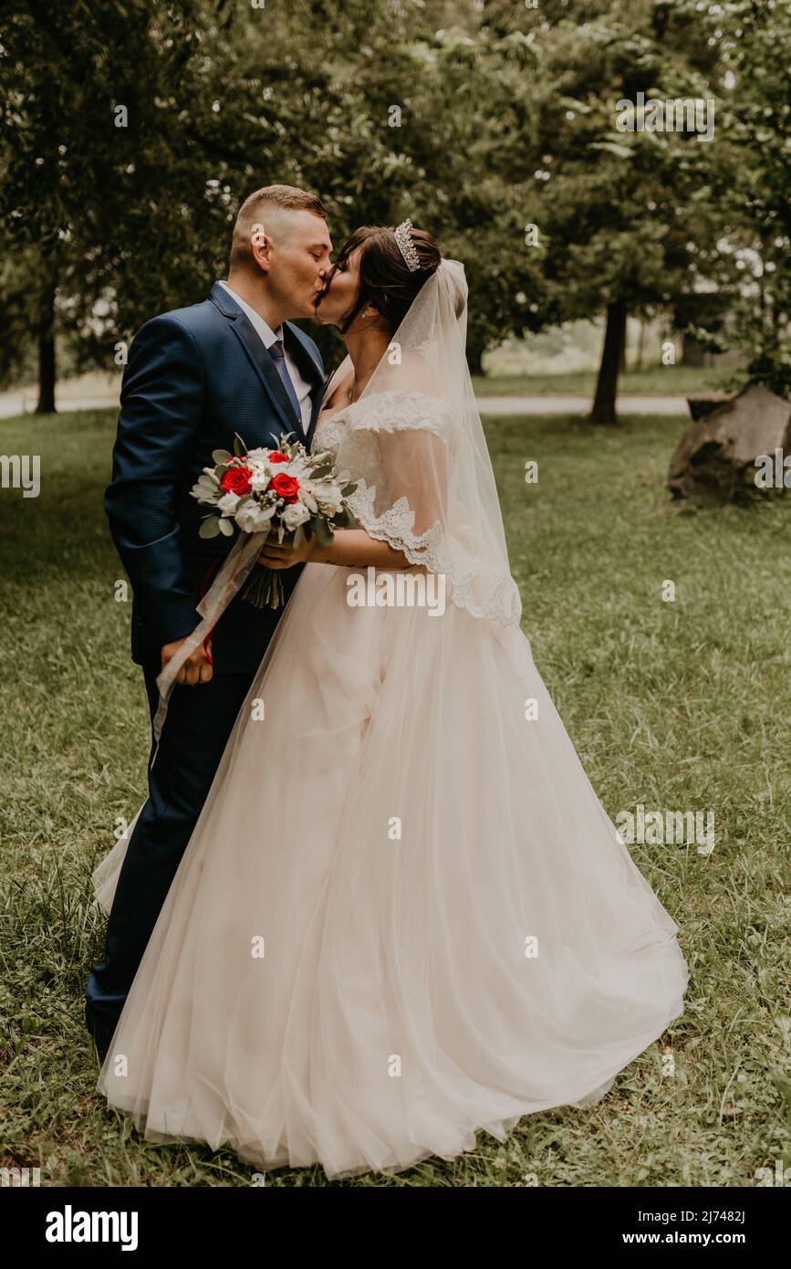 Il giovane uomo biondo caucasico europeo sposa in abito blu e donna dai capelli neri sposa in abito da sposa bianco con velo lungo e tiara sulla testa. Prima Foto Stock