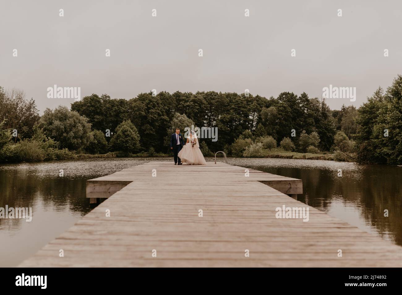 Il giovane uomo biondo caucasico europeo sposa in abito blu e donna dai capelli neri sposa in abito da sposa bianco con velo lungo e tiara sulla testa. Sposi novelli Foto Stock
