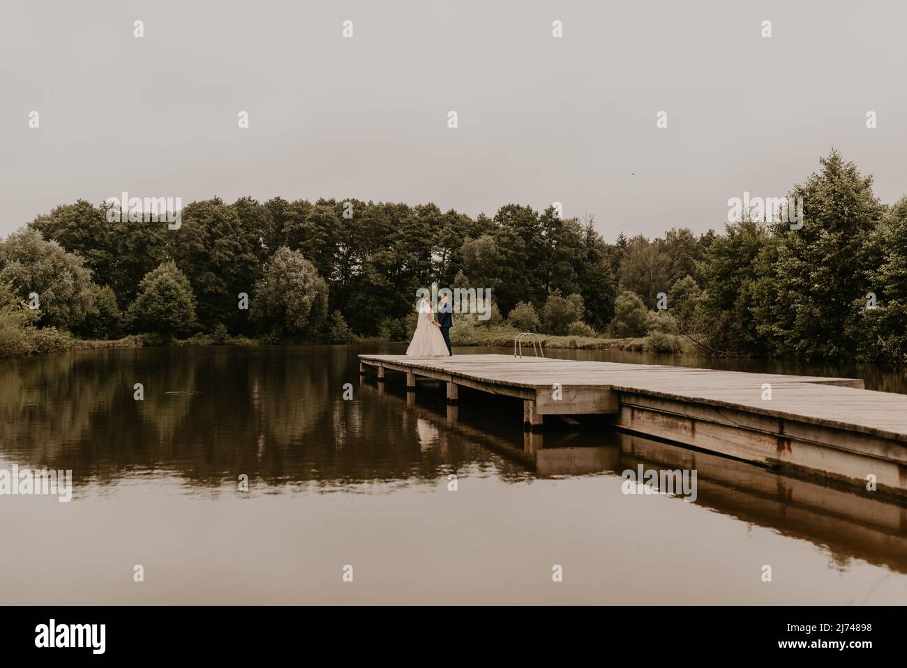 Il giovane uomo biondo caucasico europeo sposa in abito blu e donna dai capelli neri sposa in abito da sposa bianco con velo lungo e tiara sulla testa. Sposi novelli Foto Stock