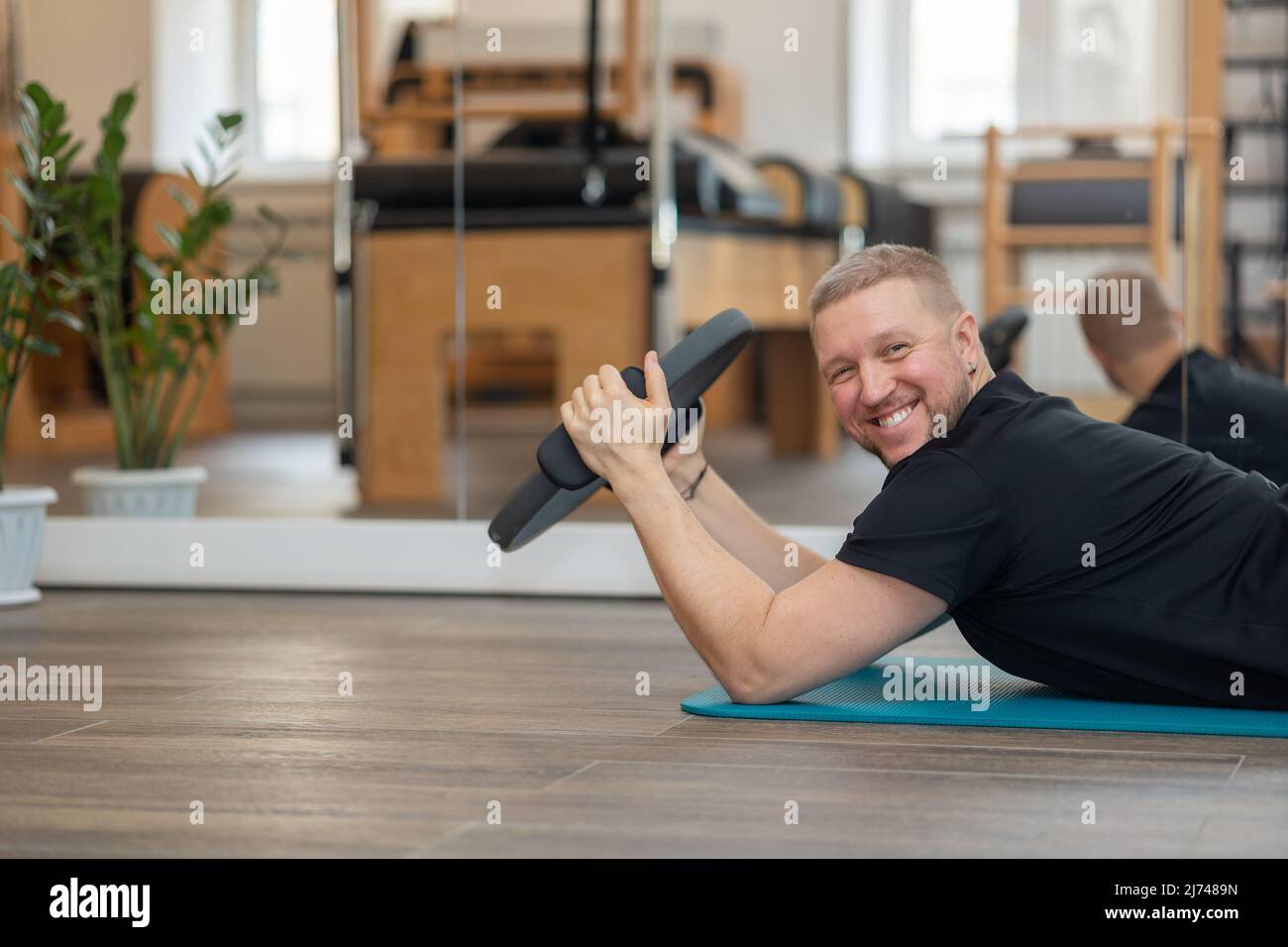 L'allenatore di pilates per il fitness maschile mostra esercizi su simulatori speciali. Anelli in gomma per l'allungamento. Foto di alta qualità Foto Stock