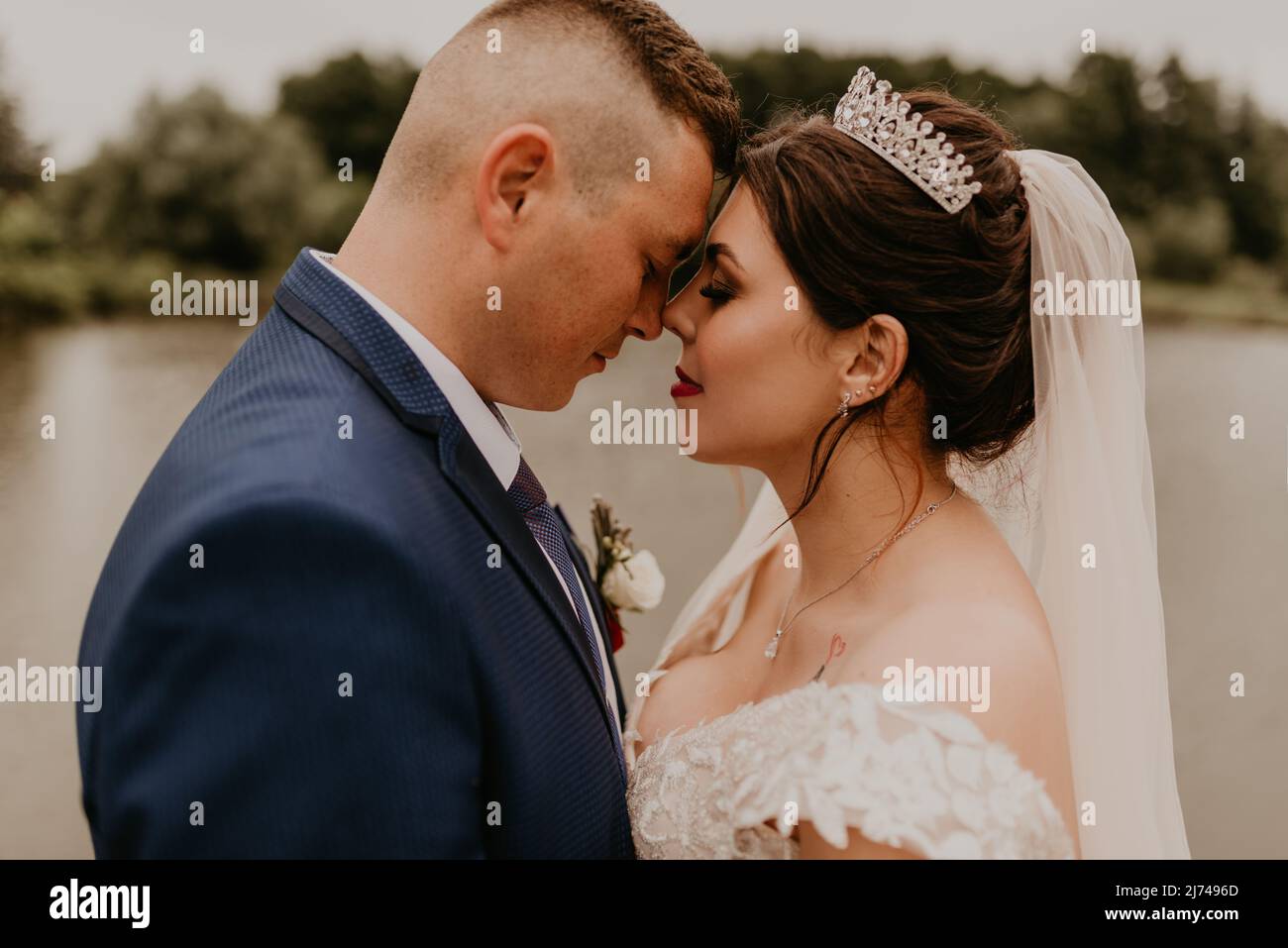 Il giovane uomo biondo caucasico europeo sposa in abito blu e donna dai capelli neri sposa in abito da sposa bianco con velo lungo e tiara sulla testa. Sposi novelli Foto Stock