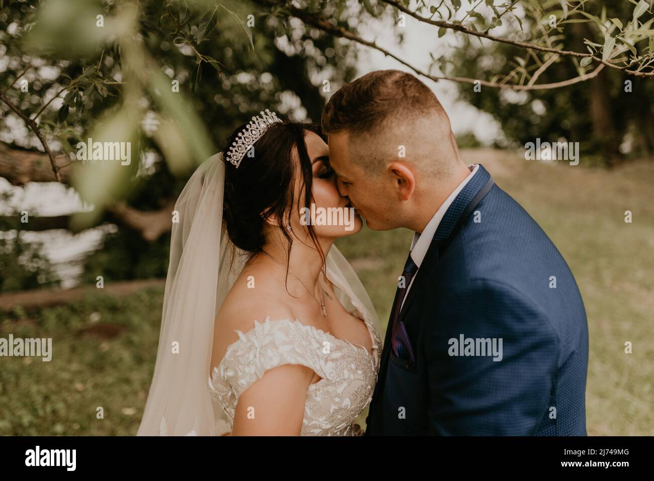 Il giovane uomo biondo caucasico europeo sposa in abito blu e donna dai capelli neri sposa in abito da sposa bianco con velo lungo e tiara sulla testa. Sposi novelli Foto Stock