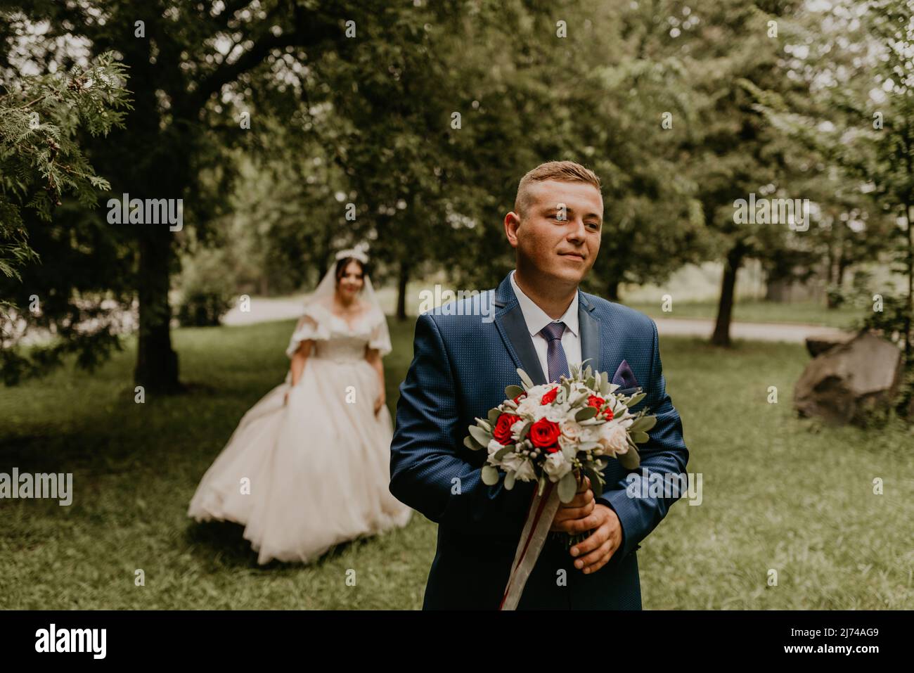 Il giovane uomo biondo caucasico europeo sposa in abito blu e donna dai capelli neri sposa in abito da sposa bianco con velo lungo e tiara sulla testa. Prima Foto Stock