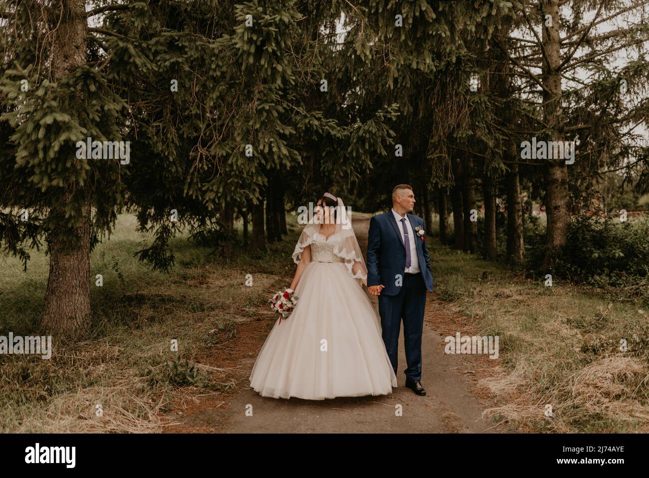 Il giovane uomo biondo caucasico europeo sposa in abito blu e donna dai capelli neri sposa in abito da sposa bianco con velo lungo e tiara sulla testa. Sposi novelli Foto Stock