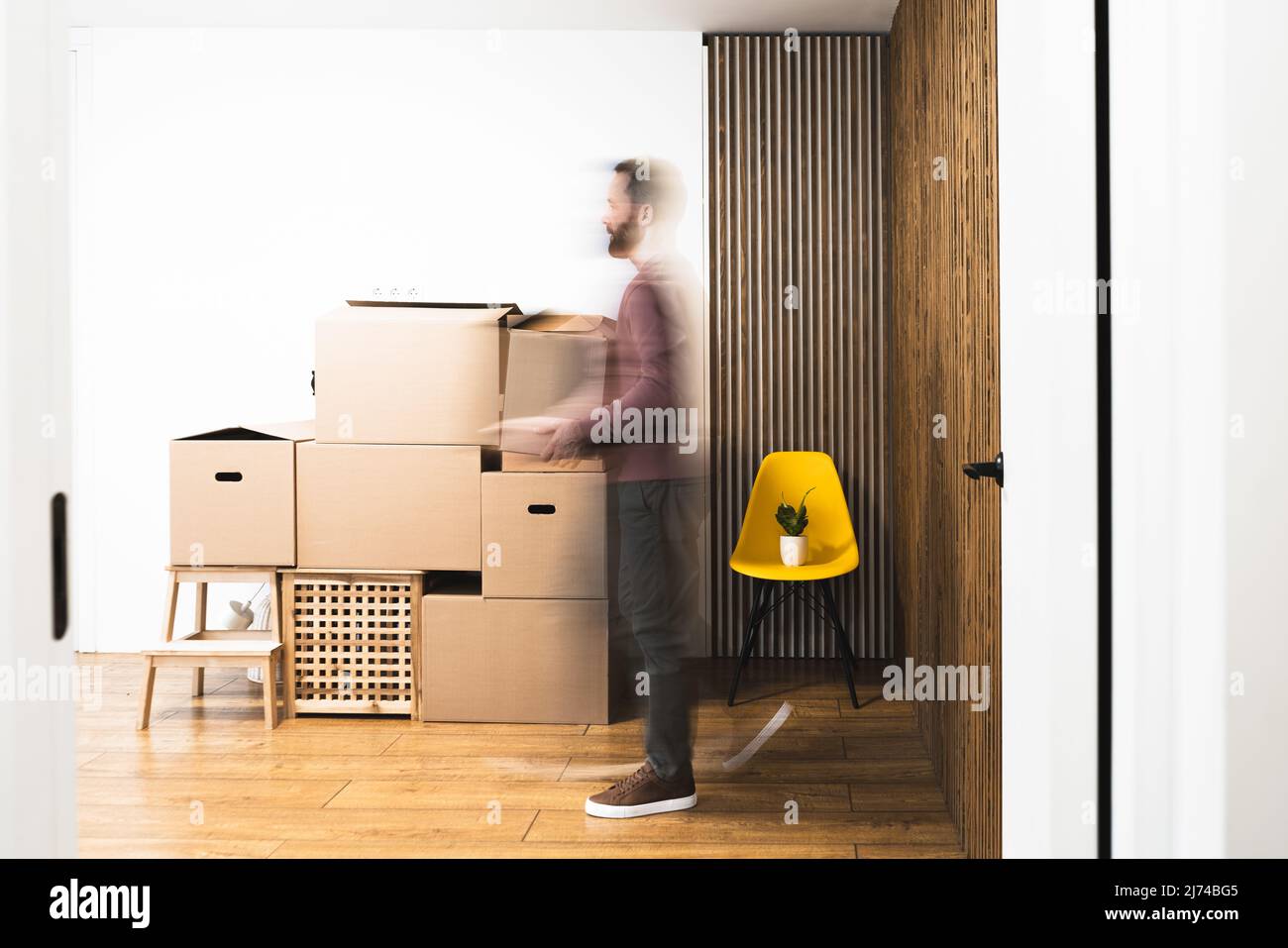 L'uomo maturo trasporta le scatole con le cose mentre si muove in appartamento nuovo non ammobiliato. Esposizione prolungata. Foto Stock