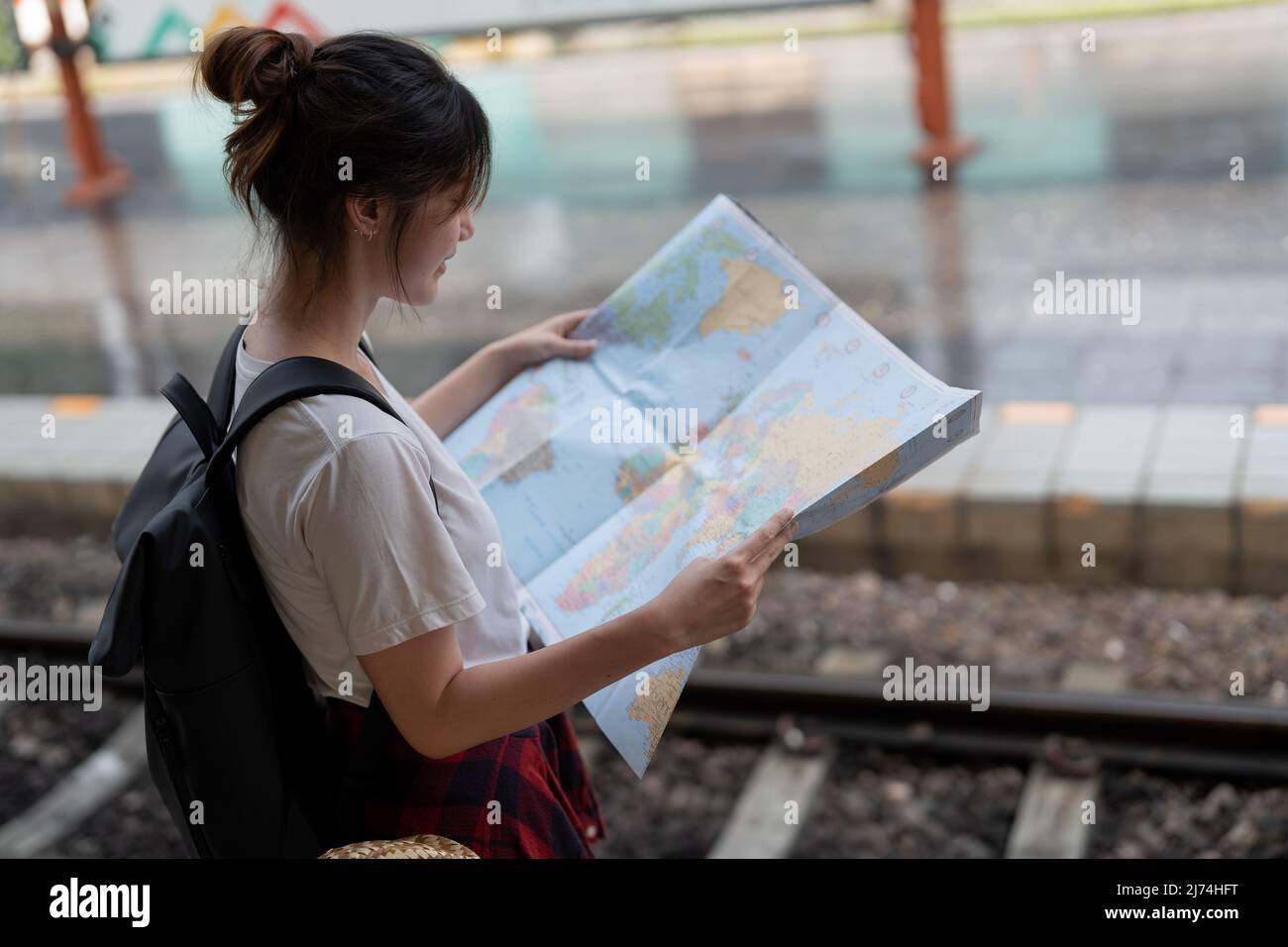 Una giovane donna viaggiatore in piedi con mappa scegliere dove viaggiare e borsa in attesa di treno alla stazione ferroviaria Foto Stock