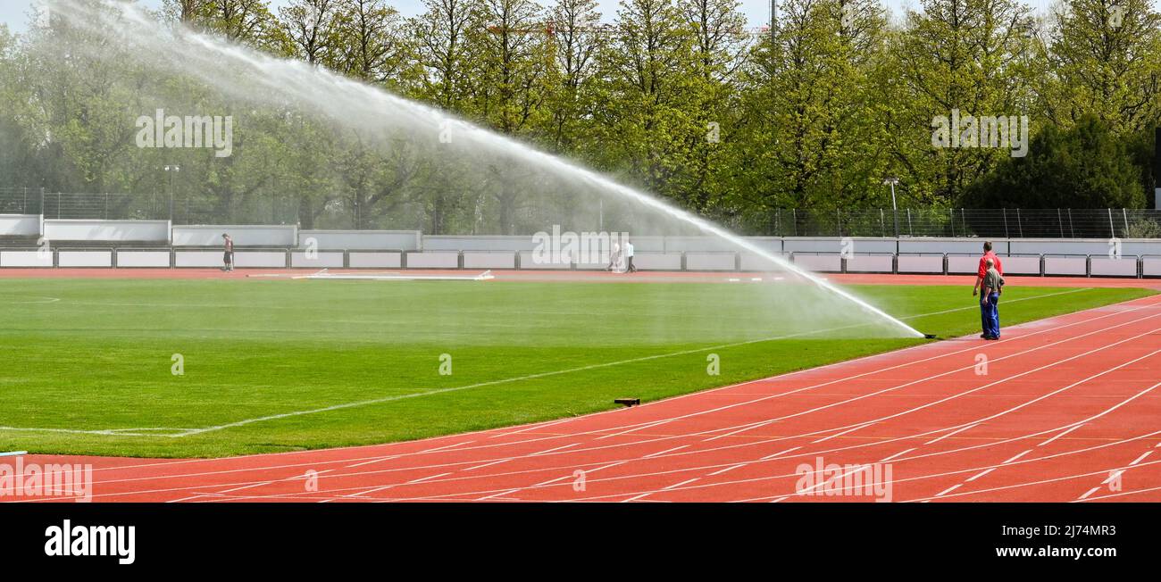Basilea, Svizzera - Aprile 2022: Groundspersons in uno stadio di atletica che utilizza un potente euipment spray per innaffiare il campo di erba. Foto Stock