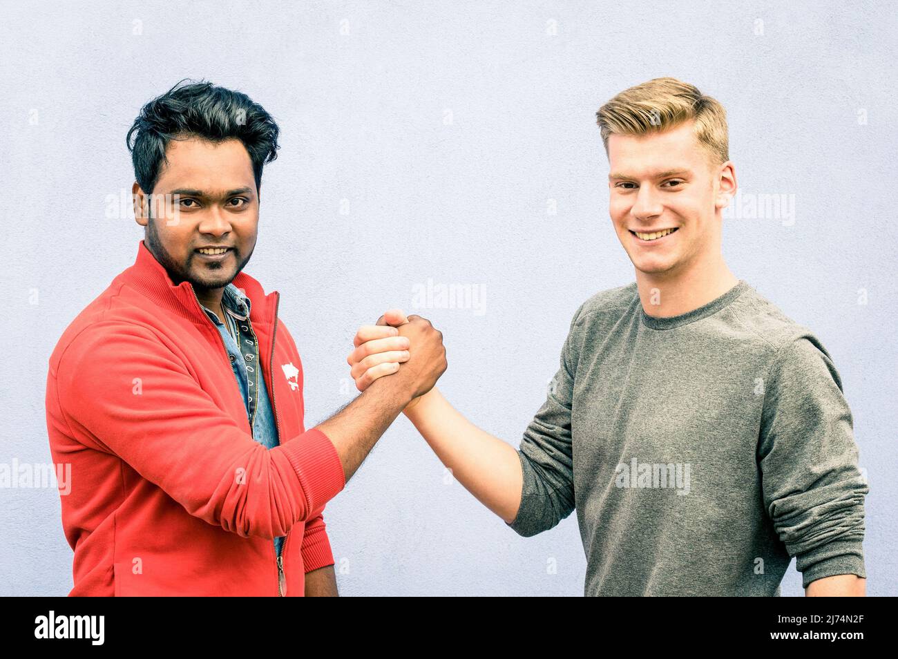 Gli uomini indiani e caucasici scuotono le mani in una stretta di mano moderna per mostrarsi amicizia e rispetto - i migliori amici che hanno braccio lottando contro rac Foto Stock