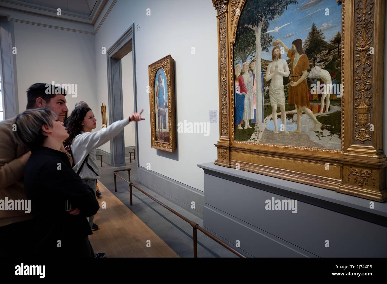 National Gallery London Inghilterra Aprile 2022 i visitatori tornano a Londra dopo i due anni di blocco di Covid che si sono visti qui alla National Gallery di Trafalgar Square nel centro di Londra. I visitatori ammirano: Il Battesimo di Cristo (centro) e San Michele (a sinistra) è un dipinto del maestro rinascimentale italiano Piero della Francesca. Dipinta in tempera d'uovo su due pannelli di legno di pioppo, la datazione è controversa – alcuni gli danno una data molto presto, forse 1439; altri molto più tardi, intorno al 1460. Si tiene presso la National Gallery di Londra. La composizione è centrata sulla figura dell'essere di Cristo Foto Stock